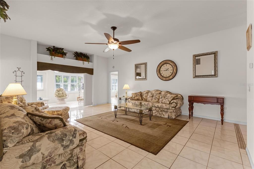 A living room with tile floors, a floral sofa, a ceiling fan, and a rug — 704 PINNACLE DRIVE, HAINES CITY, FL