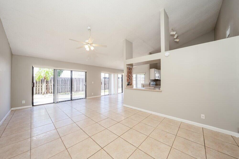 An open-concept living area features light-colored tile floors, vaulted ceilings, and a kitchen pass-through window — BOYNTON BEACH, FL