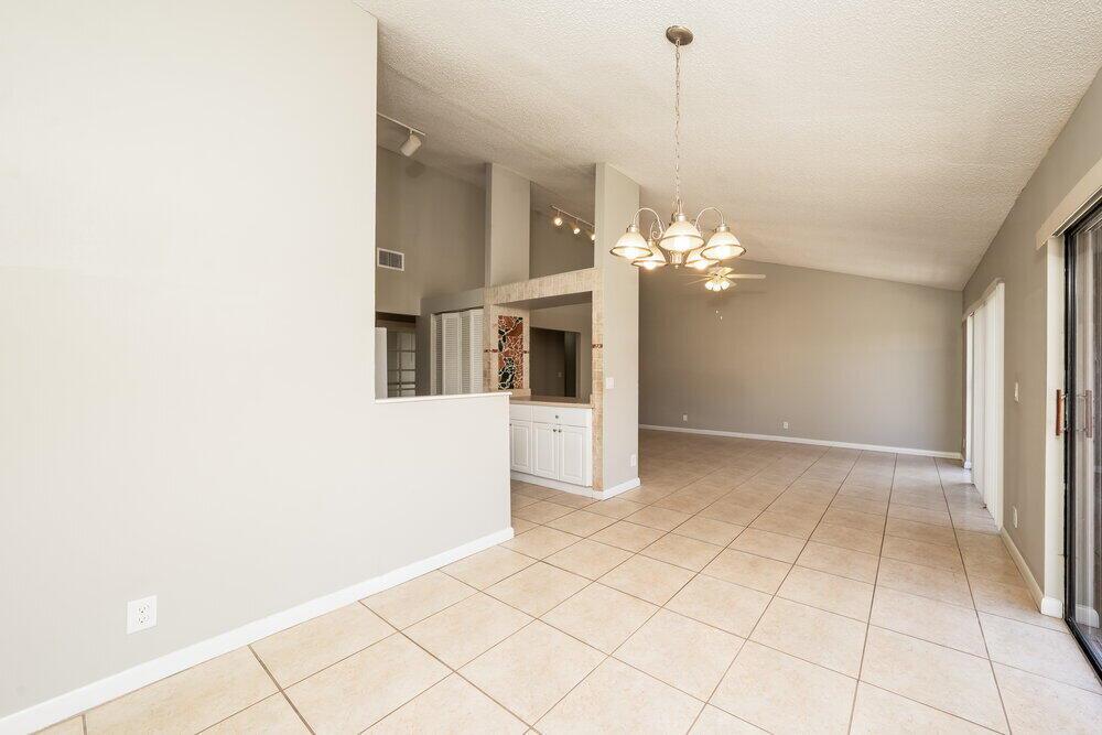 An open-concept living area features light-colored tile flooring, a vaulted ceiling, and a chandelier — BOYNTON BEACH, FL