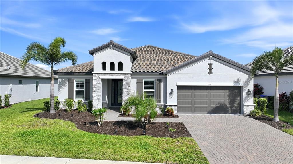A single-story house with a tiled roof, stone accents, and a paved driveway — 19857 MONTENERO WAY, VENICE, FL