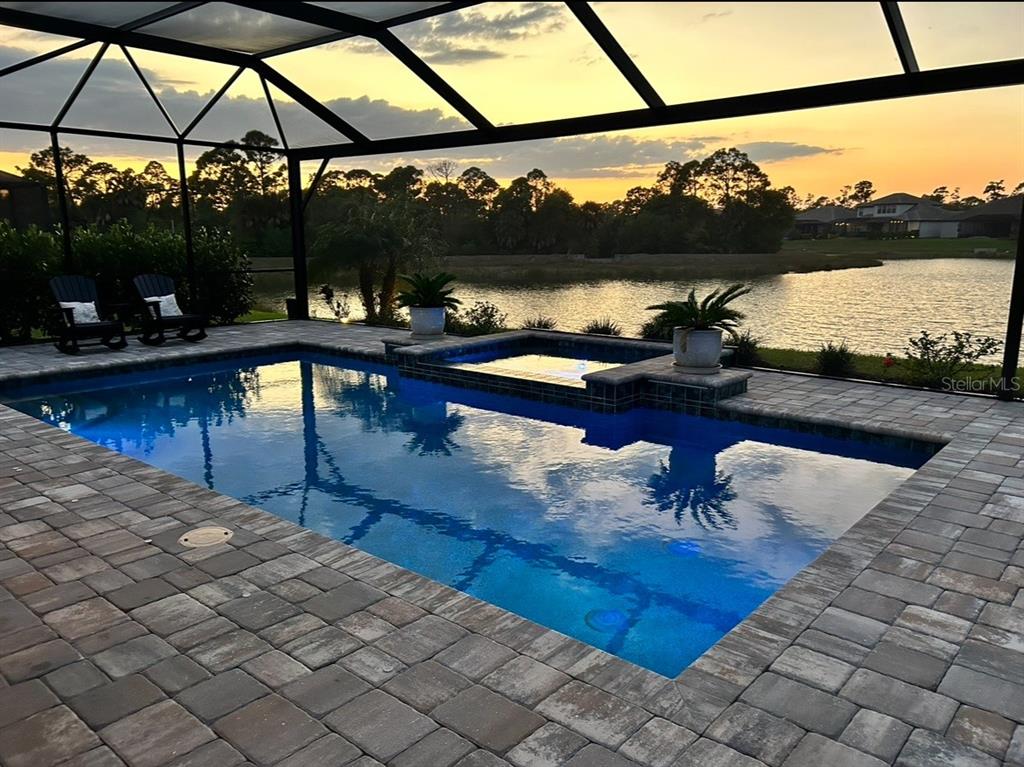 A screened-in pool and spa overlook a lake at sunset with a paver patio — 19857 MONTENERO WAY, VENICE, FL