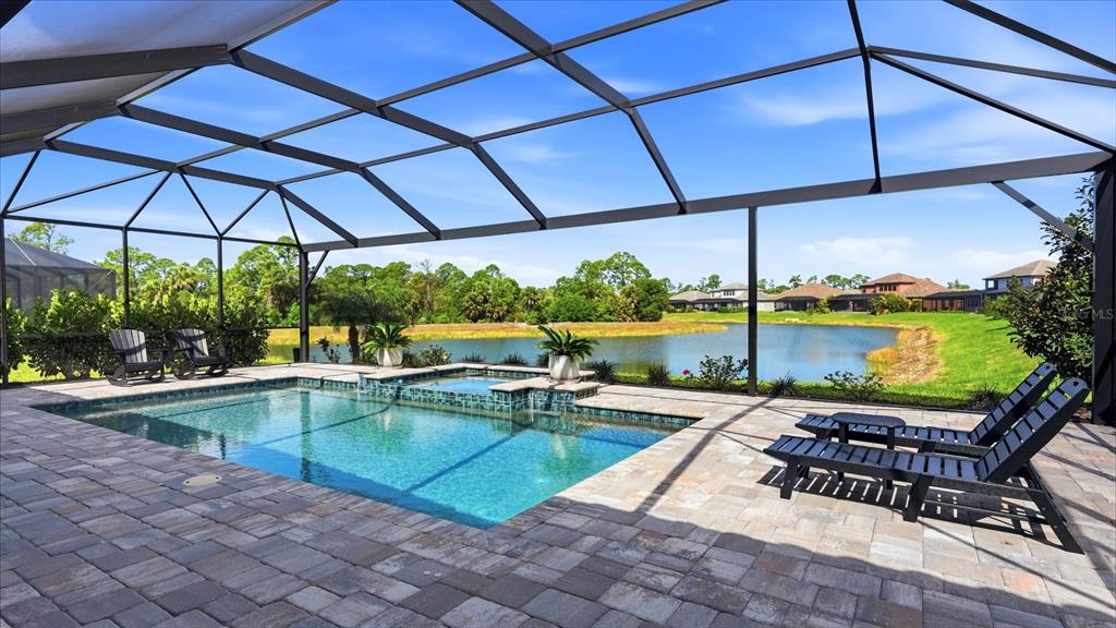 A screened-in pool and spa overlook a lake with houses in the background — 19857 MONTENERO WAY, VENICE, FL