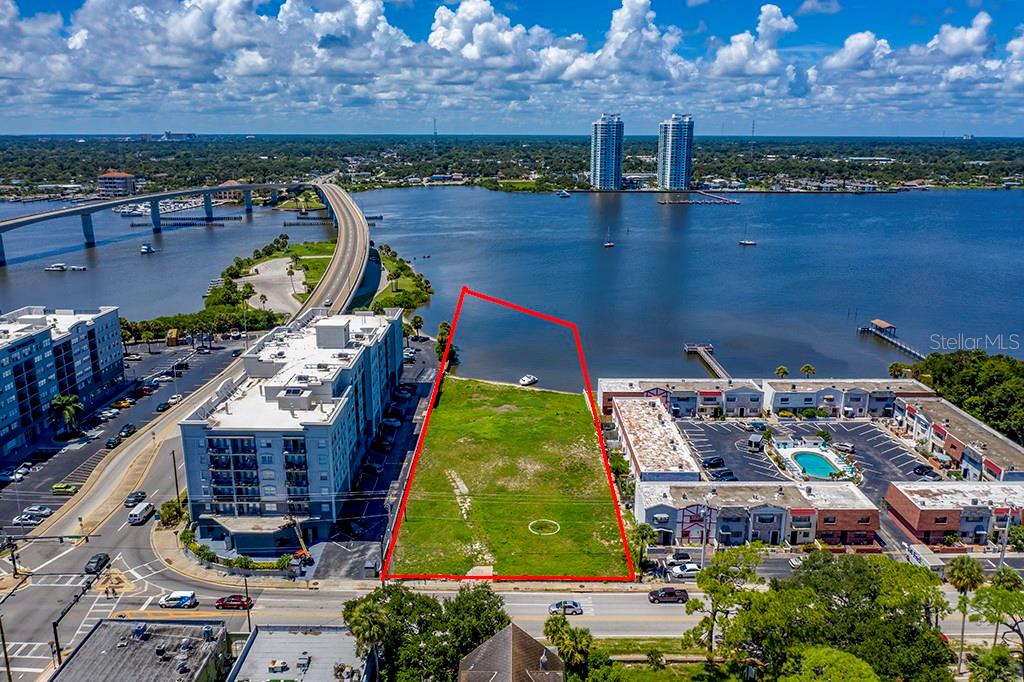 An aerial view shows a vacant waterfront lot outlined in red between two apartment complexes — 613 HALIFAX AVENUE, DAYTONA BEACH, FL