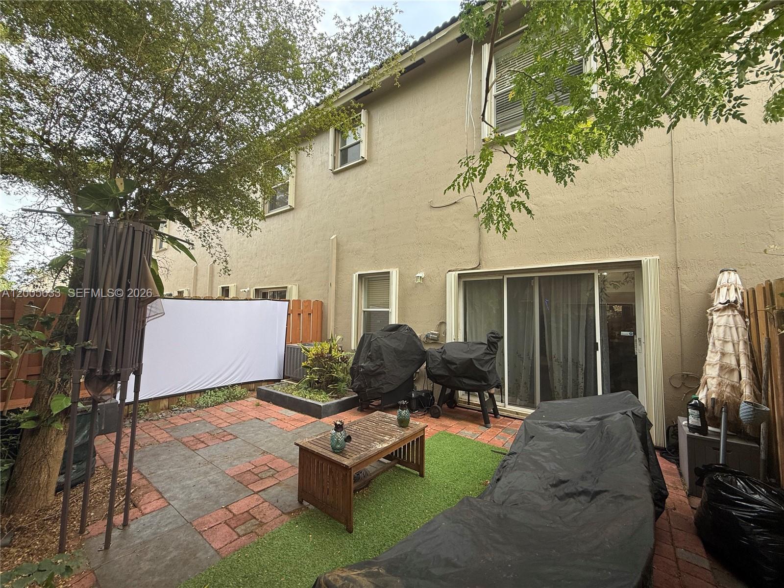 A backyard patio features a paved area, artificial turf, a wooden table, and outdoor furniture — 8979 SW 225th St, Cutler Bay FL 33190, CUTLER BAY, FL