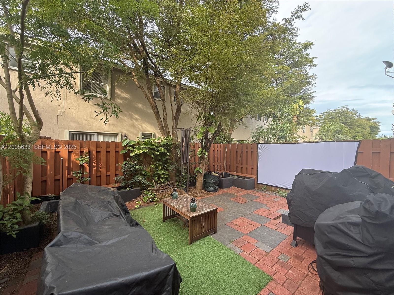 A fenced backyard features a brick patio, artificial turf, a wooden table, and a projector screen — 8979 SW 225th St, Cutler Bay FL 33190, CUTLER BAY, FL