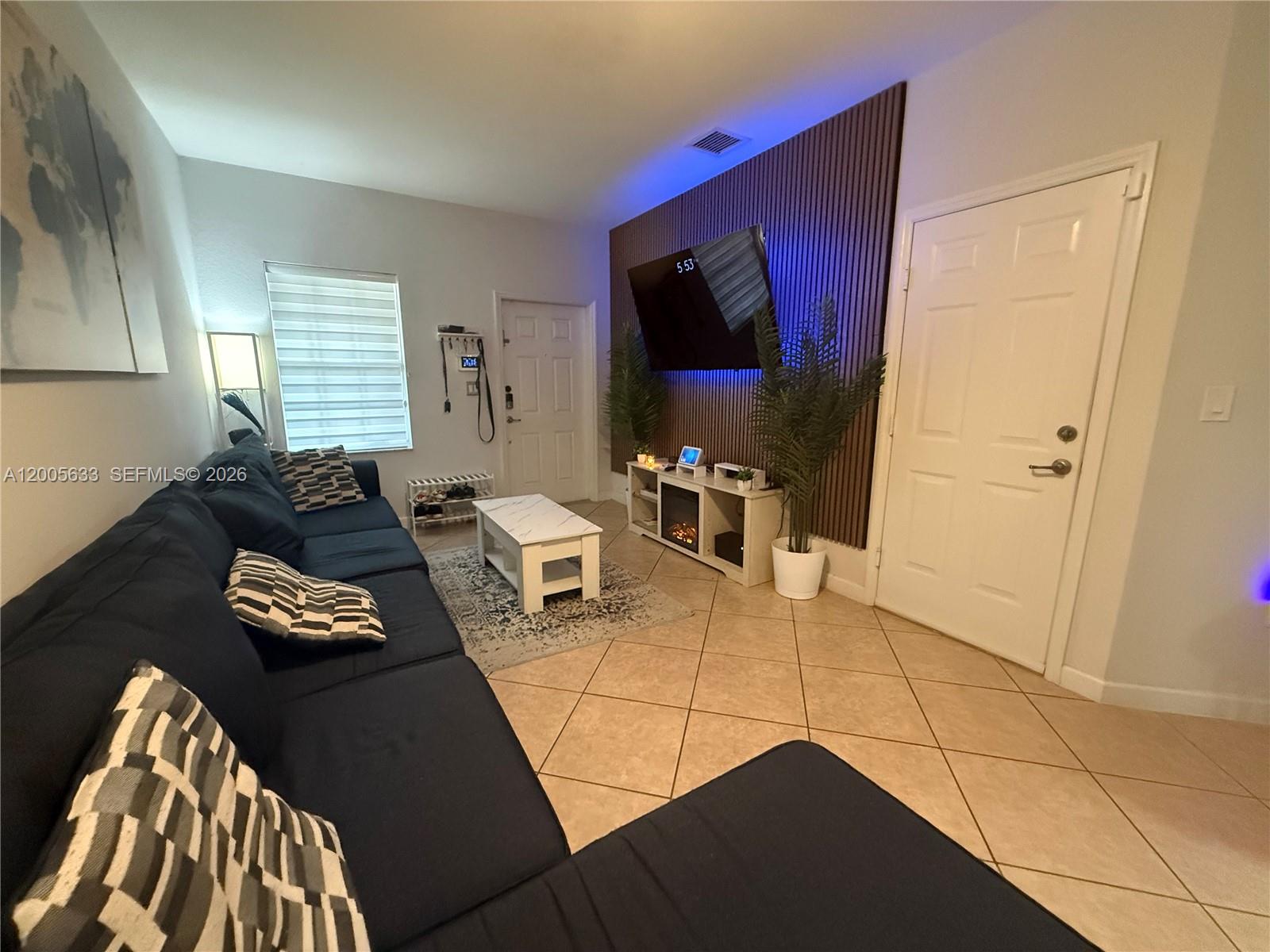 A living room features a dark blue sectional sofa, a wall-mounted television, and wood-slat paneling — 8979 SW 225th St, Cutler Bay FL 33190, CUTLER BAY, FL