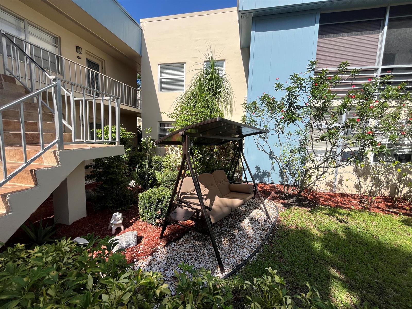 A patio swing sits on a gravel bed in a courtyard between two apartment buildings — 897 Flanders S # 897, Delray Beach FL 33484, DELRAY BEACH, FL