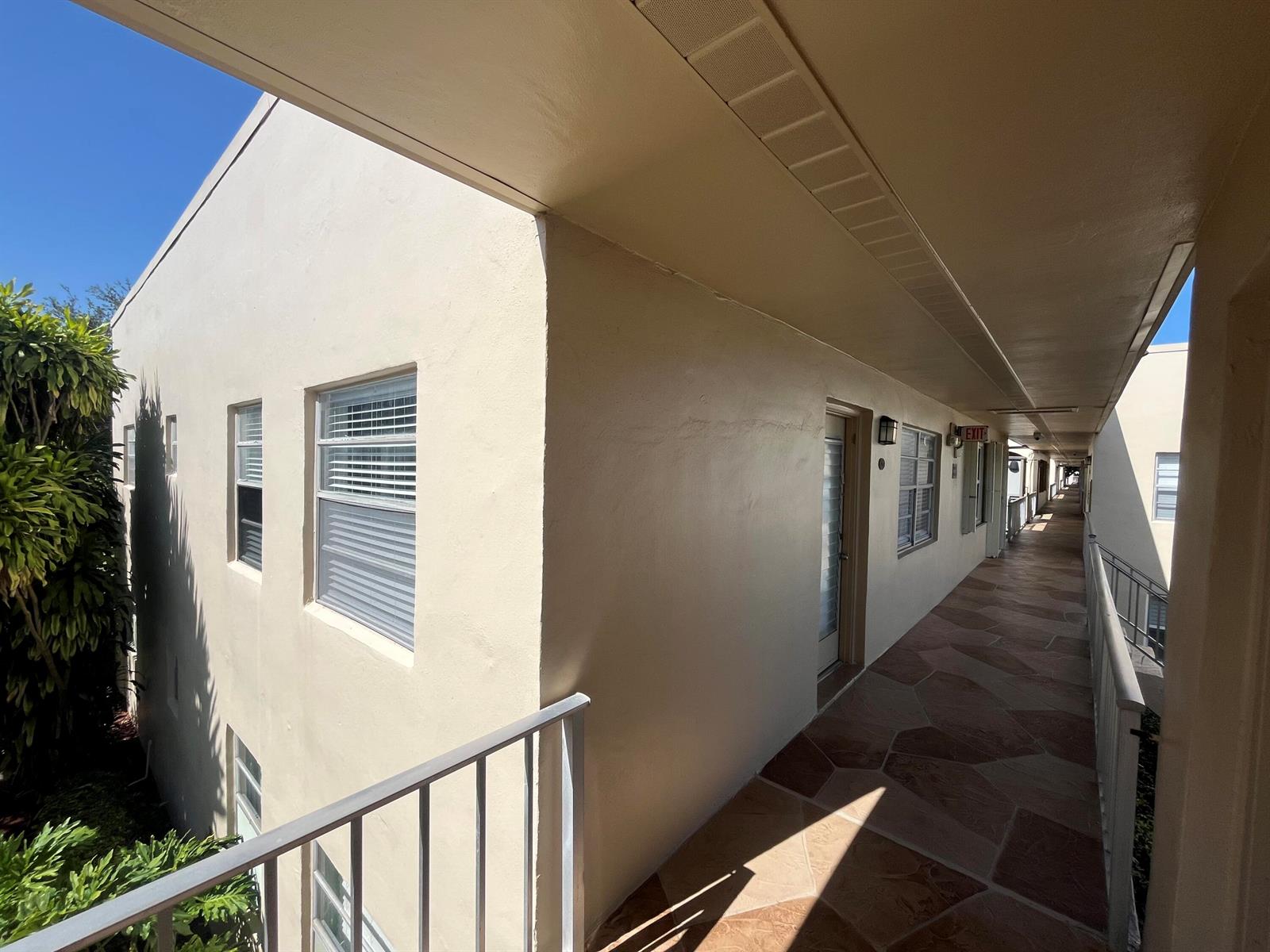 An exterior walkway with tiled flooring leads past apartment doors along a beige building — 897 Flanders S # 897, Delray Beach FL 33484, DELRAY BEACH, FL