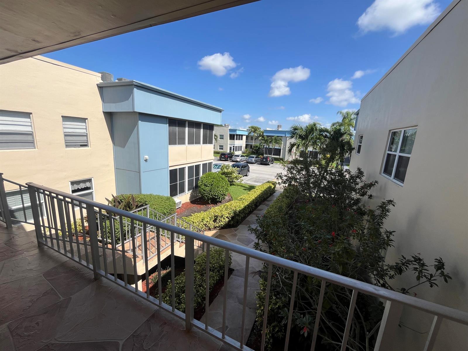 A view from a balcony overlooking a courtyard with landscaping, walkways, and apartment buildings — 897 Flanders S # 897, Delray Beach FL 33484, DELRAY BEACH, FL
