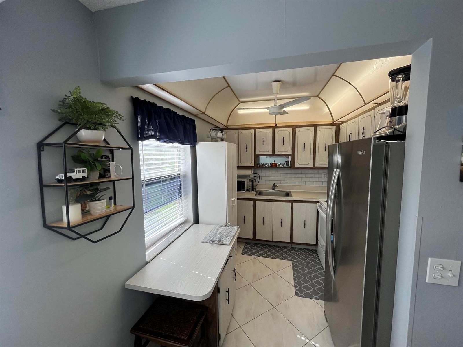 A kitchen features light-colored cabinets, stainless steel appliances, a breakfast bar, and a ceiling fan — 897 Flanders S # 897, Delray Beach FL 33484, DELRAY BEACH, FL