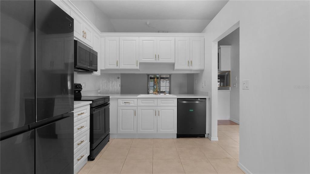 A kitchen features white cabinets, black appliances, a white countertop, and light-colored tile flooring — 3744 GATEWOOD DRIVE, PORT ORANGE, FL