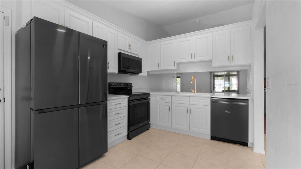 A kitchen with white cabinets, black appliances, a mirrored backsplash, and light-colored tile flooring — 3744 GATEWOOD DRIVE, PORT ORANGE, FL