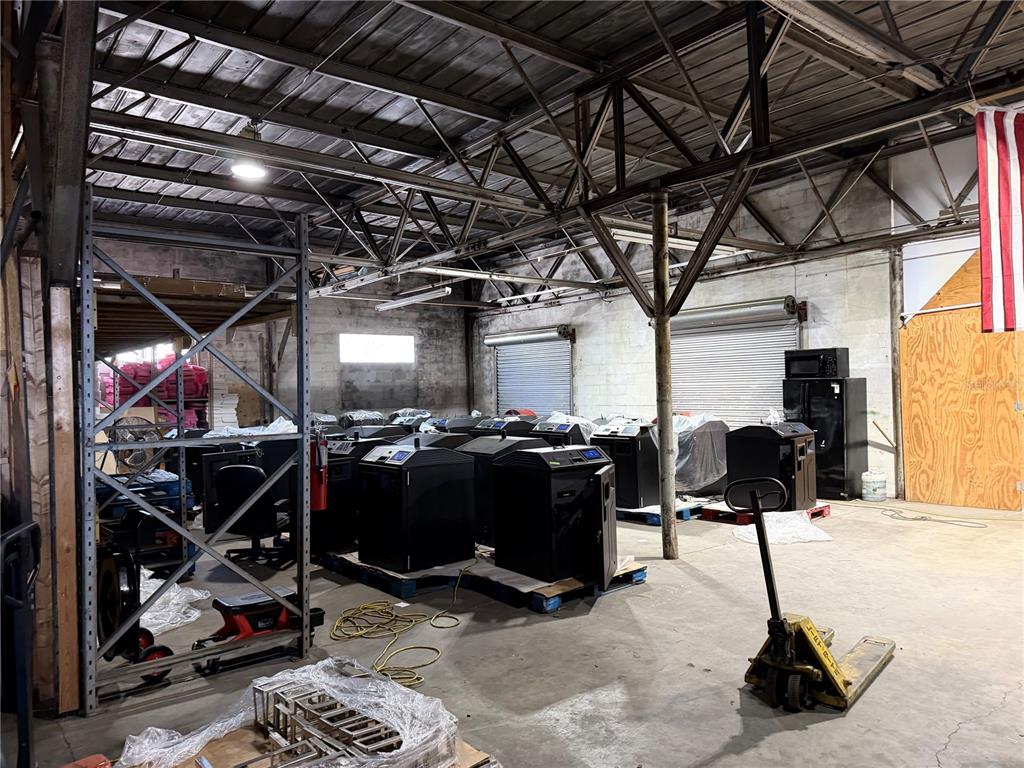 A warehouse interior features concrete floors, exposed metal trusses, and several black industrial machines on pallets — 4320 S MANHATTAN AVENUE, TAMPA, FL