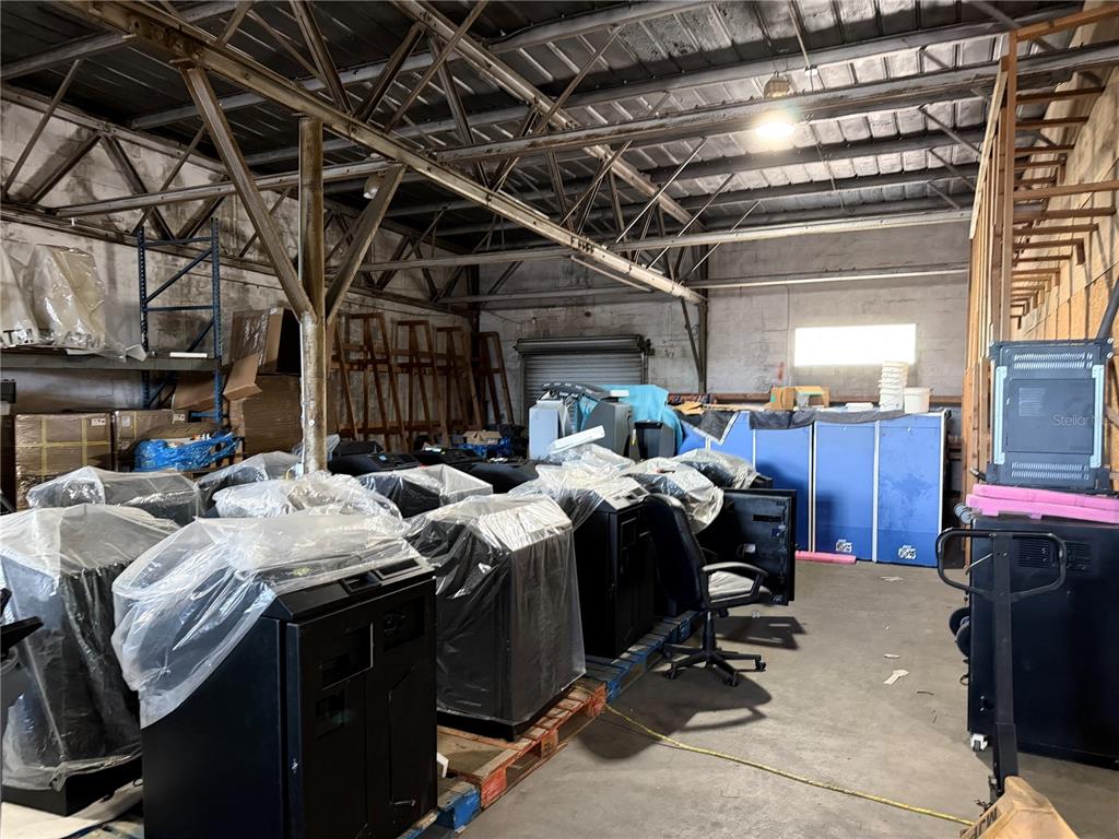 An industrial warehouse interior features exposed metal trusses, concrete walls, and rows of covered equipment — 4320 S MANHATTAN AVENUE, TAMPA, FL