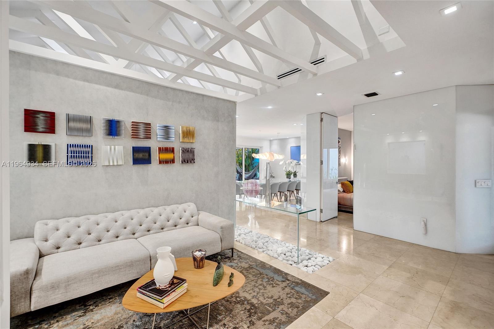 A modern living room features a tufted sofa, geometric wall art, and a vaulted ceiling — 1662 Diplomat Dr, Miami FL 33179, MIAMI, FL
