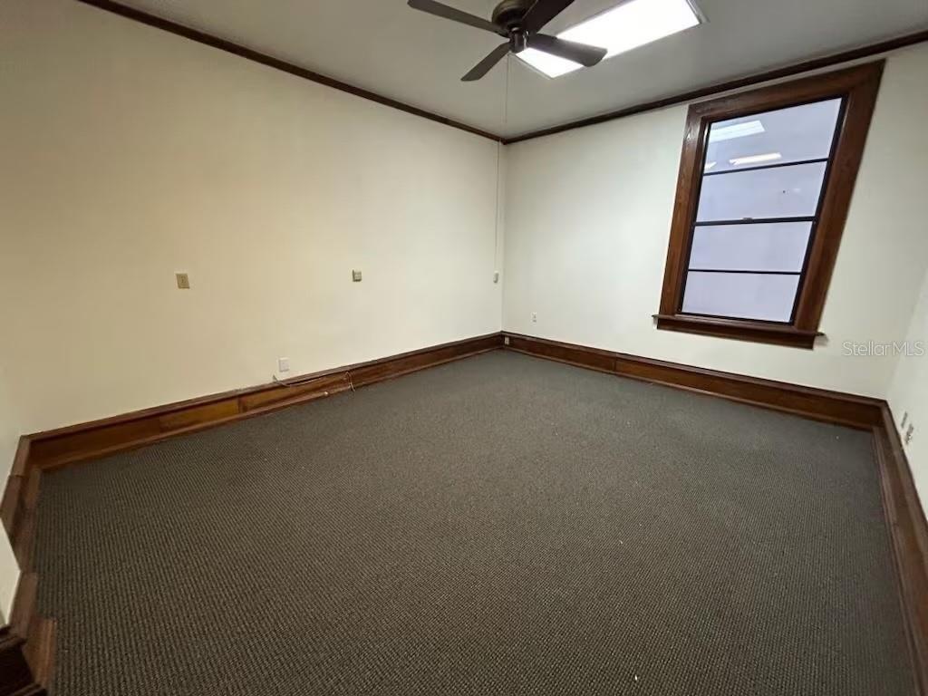 An empty room features dark carpet, wood baseboards, a ceiling fan, and a multi-pane window — 44 SE 1ST AVENUE, OCALA, FL