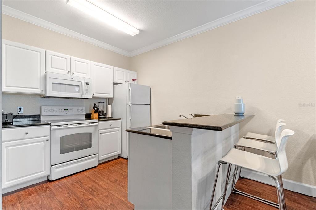A kitchen features white cabinetry, white appliances, dark countertops, and a breakfast bar with stools — 2952 LUCAYAN HARBOUR CIRCLE UNIT 106, KISSIMMEE, FL