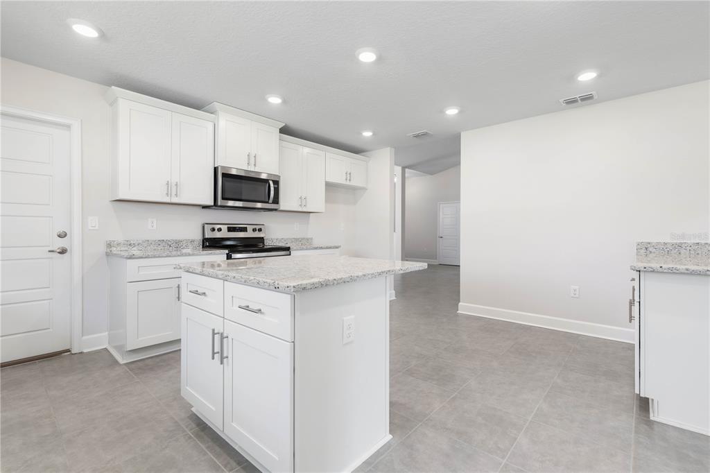 A kitchen with white cabinets, granite countertops, a center island, and gray tile flooring — 424 UNDERWOOD TRAIL, PALM COAST, FL