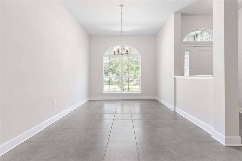 An empty dining room features gray tile flooring, a chandelier, and a large arched window — 424 UNDERWOOD TRAIL, PALM COAST, FL