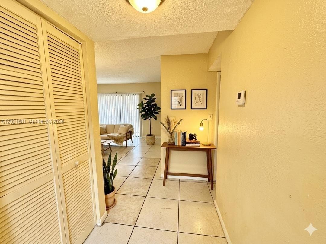 A hallway with tile flooring leads into a living area with a sofa and plant — 17650 NW 68th Ave # A2005, Hialeah FL 33015, HIALEAH, FL