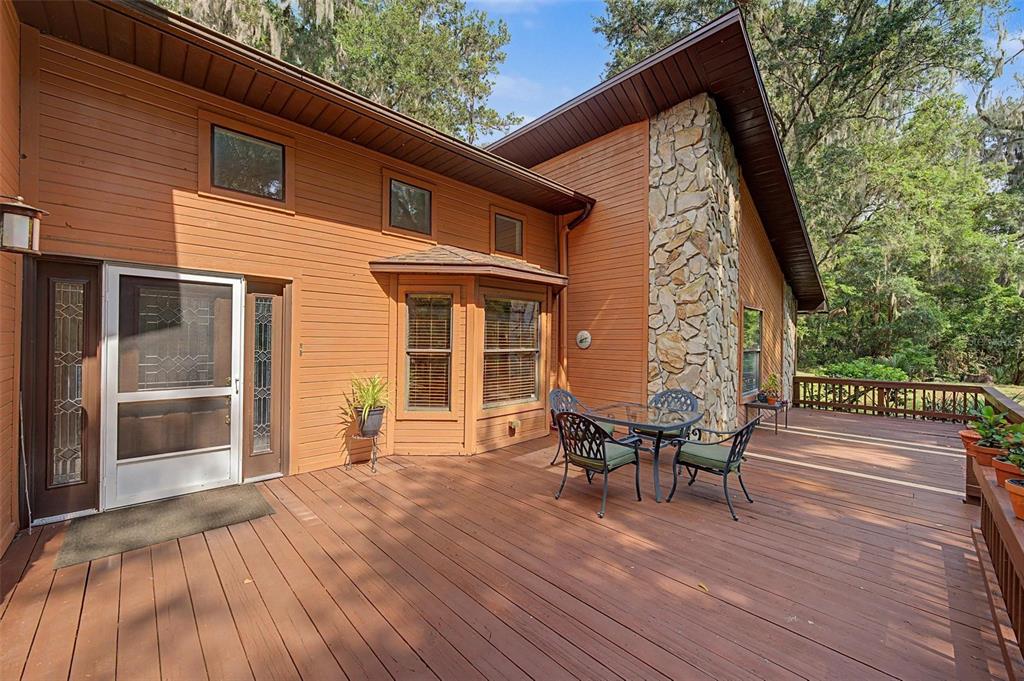 A wooden deck features a dining set, stone chimney, and a house with orange siding — 24075 WINDING CREEK DRIVE, BROOKSVILLE, FL
