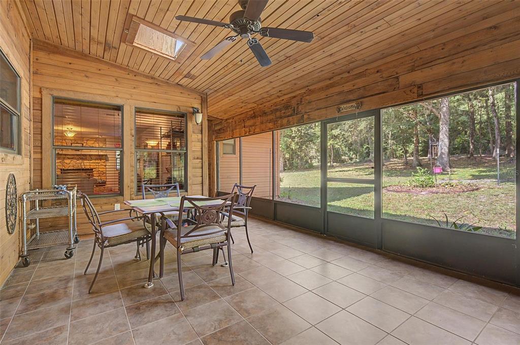 A screened-in porch with wood-paneled walls, a ceiling fan, tiled floors, and outdoor views — 24075 WINDING CREEK DRIVE, BROOKSVILLE, FL