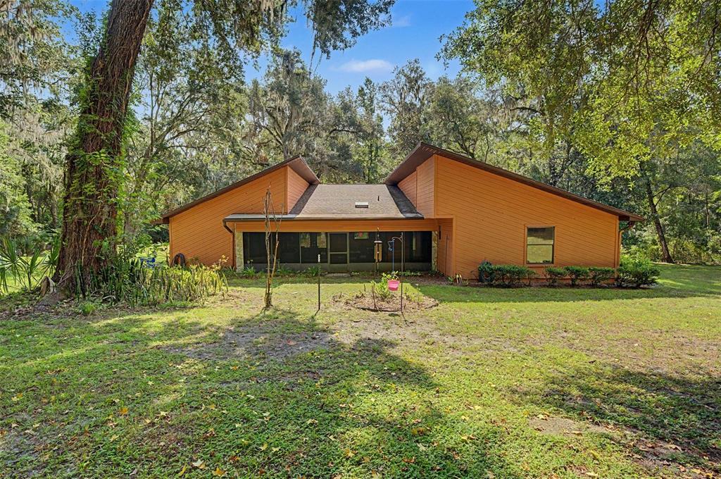 A single-story house with orange siding and a screened-in porch sits in a wooded yard — 24075 WINDING CREEK DRIVE, BROOKSVILLE, FL