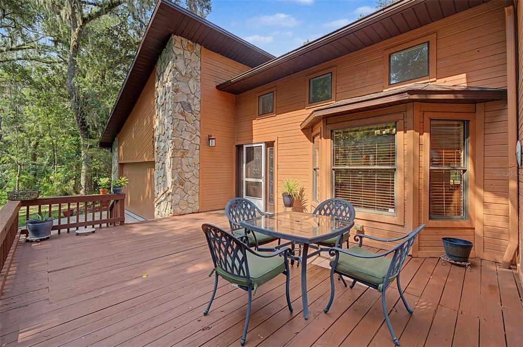 A wooden deck with patio furniture sits outside a house with brown siding and stone — 24075 WINDING CREEK DRIVE, BROOKSVILLE, FL