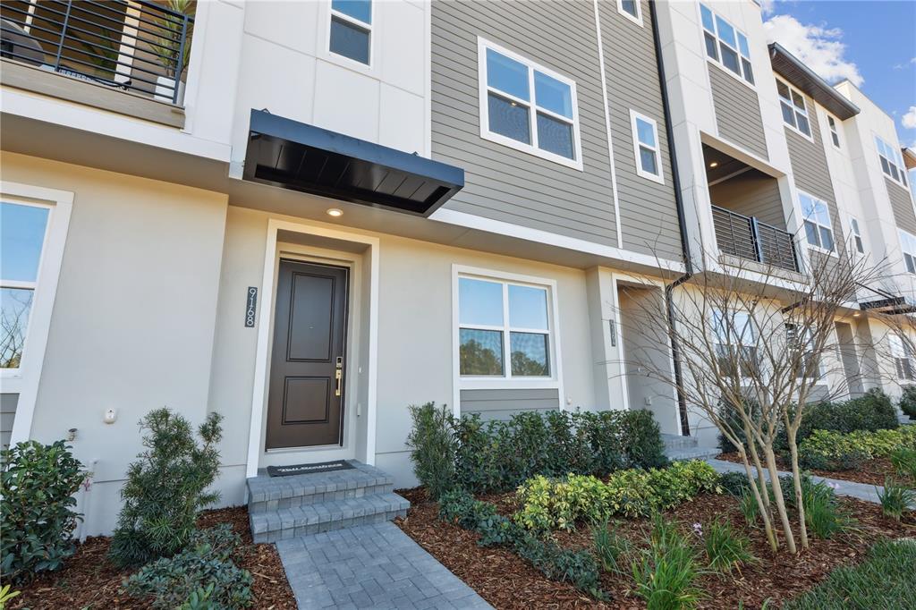 The exterior of a modern multi-story townhouse features a dark door and gray siding — 9168 SINATRA LANE, ORLANDO, FL