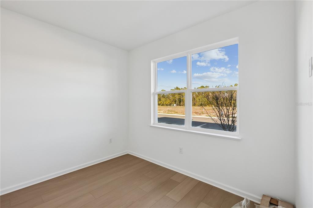 An empty room with white walls, light wood-look flooring, and a window overlooking a field — 9168 SINATRA LANE, ORLANDO, FL