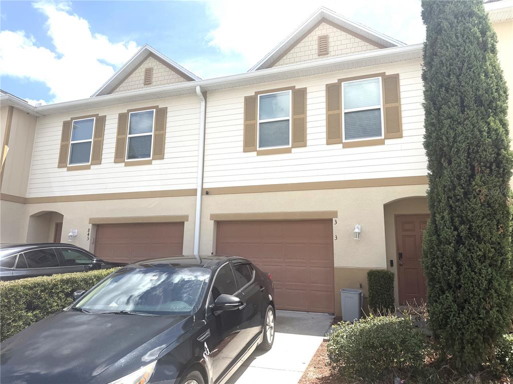 A two-story townhouse exterior features tan stucco, beige siding, brown garage doors, and a driveway — 3843 EXETER LANE, LAKELAND, FL