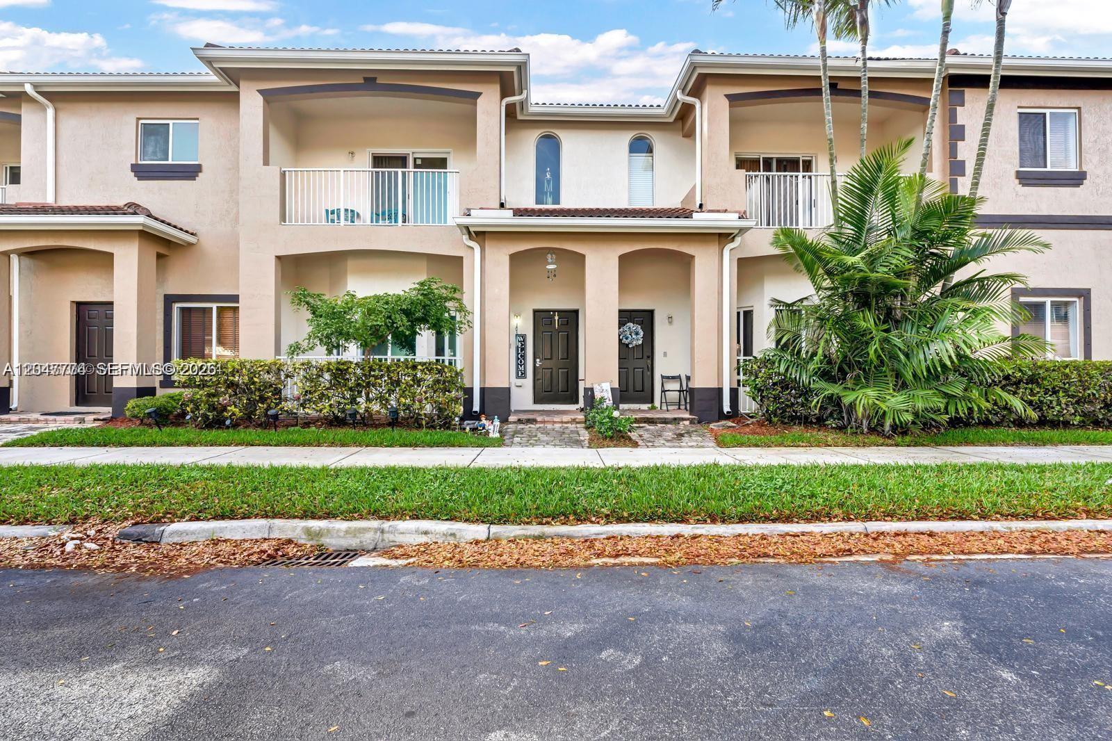 The exterior of a two-story townhouse complex features beige stucco walls, dark doors, and balconies — 1942 SE 23rd Ter, Homestead FL 33035, HOMESTEAD, FL
