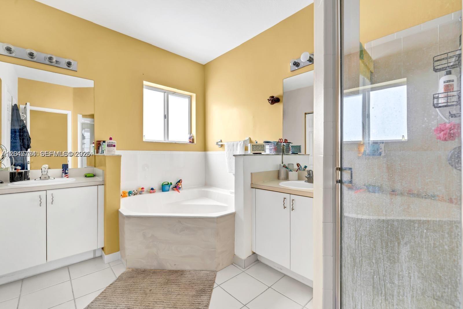 A bathroom features two white vanities, a corner soaking tub, and a glass-enclosed shower — 1942 SE 23rd Ter, Homestead FL 33035, HOMESTEAD, FL