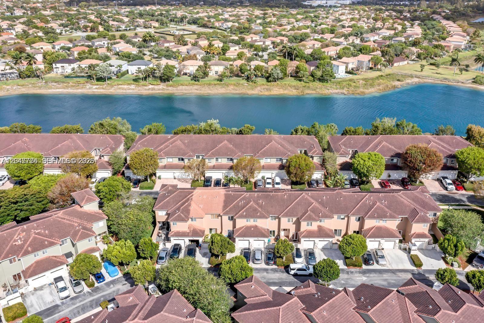 An aerial view shows multiple rows of townhomes with brown roofs near a canal — 1942 SE 23rd Ter, Homestead FL 33035, HOMESTEAD, FL