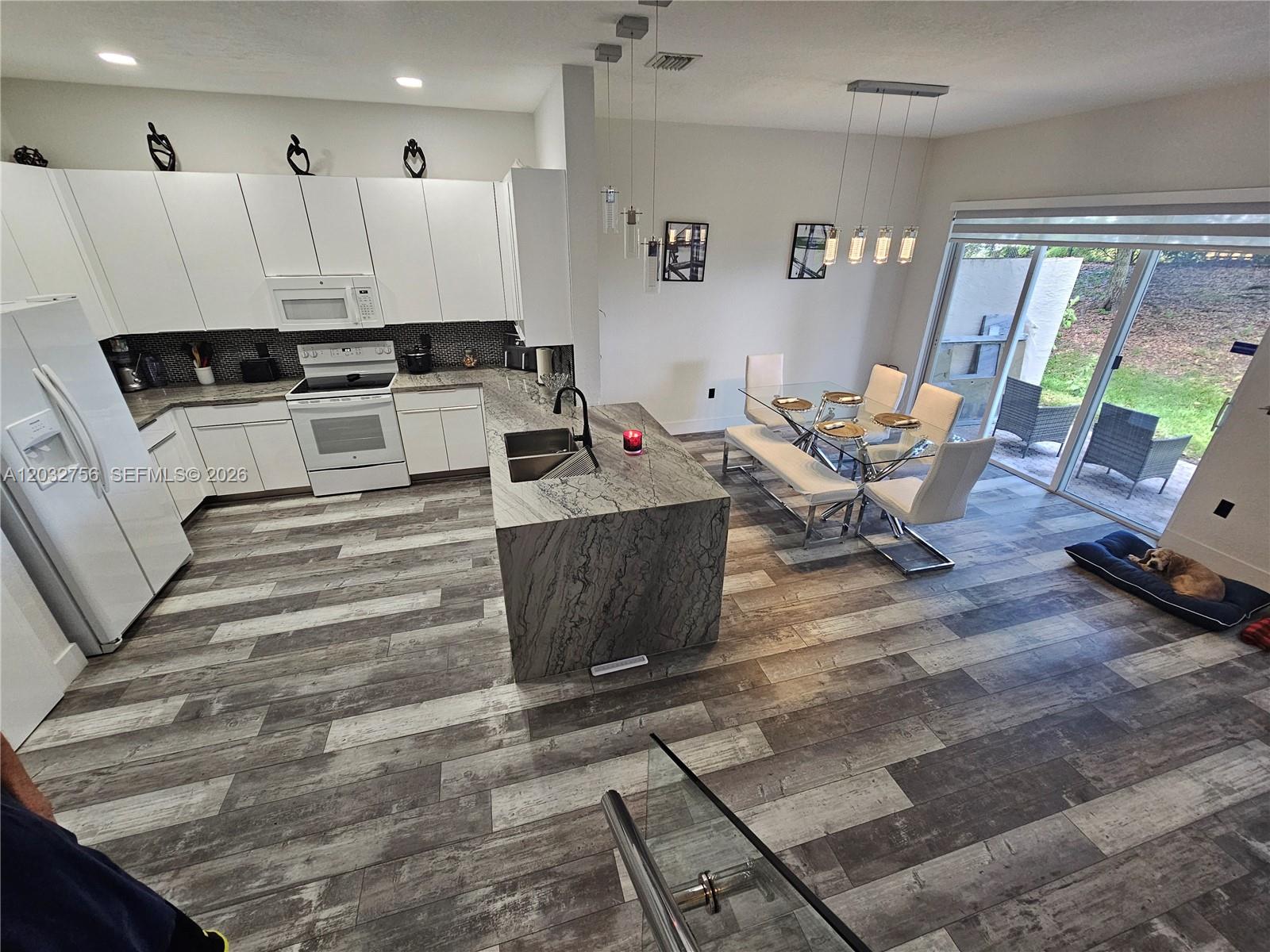 A modern kitchen with white cabinets and a stone island overlooks a dining area — 4331 SW 124th Way, Miramar FL 33027, MIRAMAR, FL