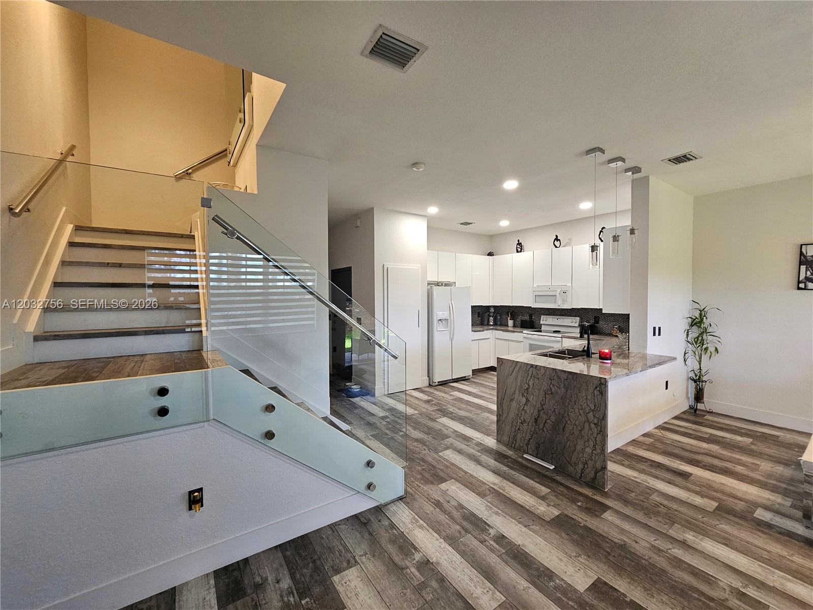 A modern kitchen features white cabinetry, a stone-topped island, and wood-look flooring near stairs — 4331 SW 124th Way, Miramar FL 33027, MIRAMAR, FL