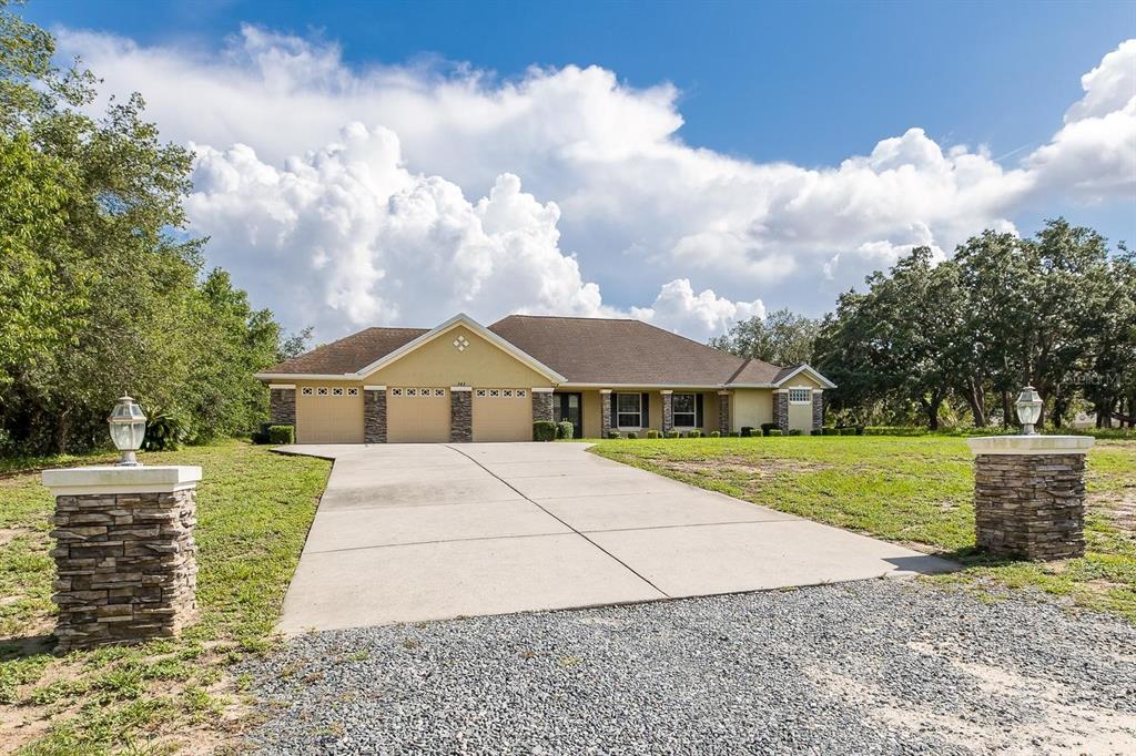 A single-story house with a three-car garage and stone accents sits behind a concrete driveway — 343 ROYAL PALM WAY, SPRING HILL, FL
