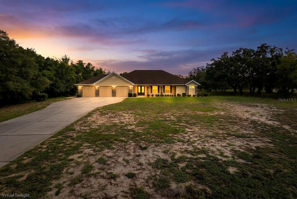 A single-story house with a three-car garage sits on a large, grassy lot at twilight — 343 ROYAL PALM WAY, SPRING HILL, FL