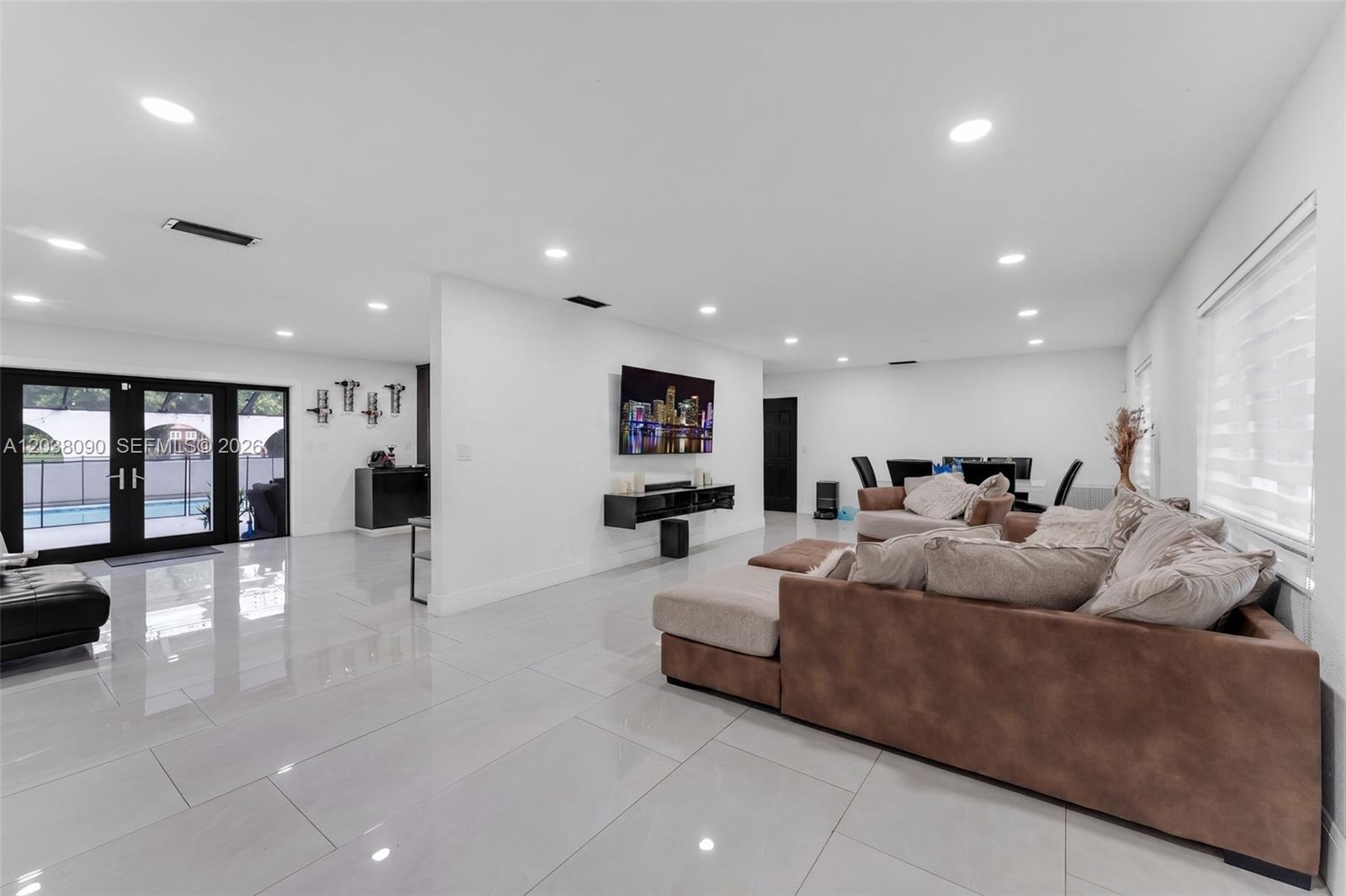 A spacious living room features white tile floors, a brown sectional sofa, and a wall-mounted television — 551 SW 127th Ave, Miami FL 33184, MIAMI, FL
