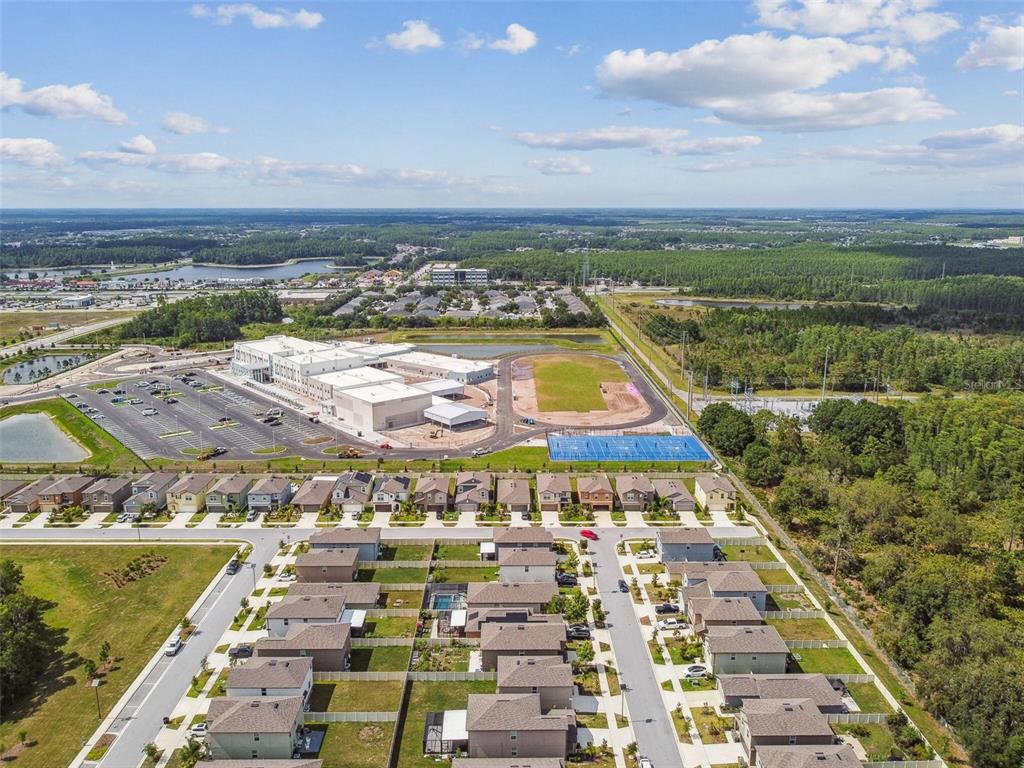 An aerial view shows a suburban neighborhood adjacent to a large school complex and forest — 2139 STELLAR BRILLIANCE WAY, LUTZ, FL