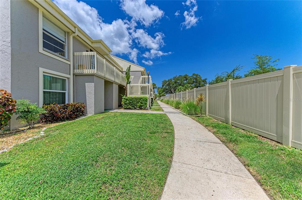 A concrete walkway runs alongside a multi-story apartment building and a tall privacy fence — 5962 7TH AVE W, BRADENTON, FL