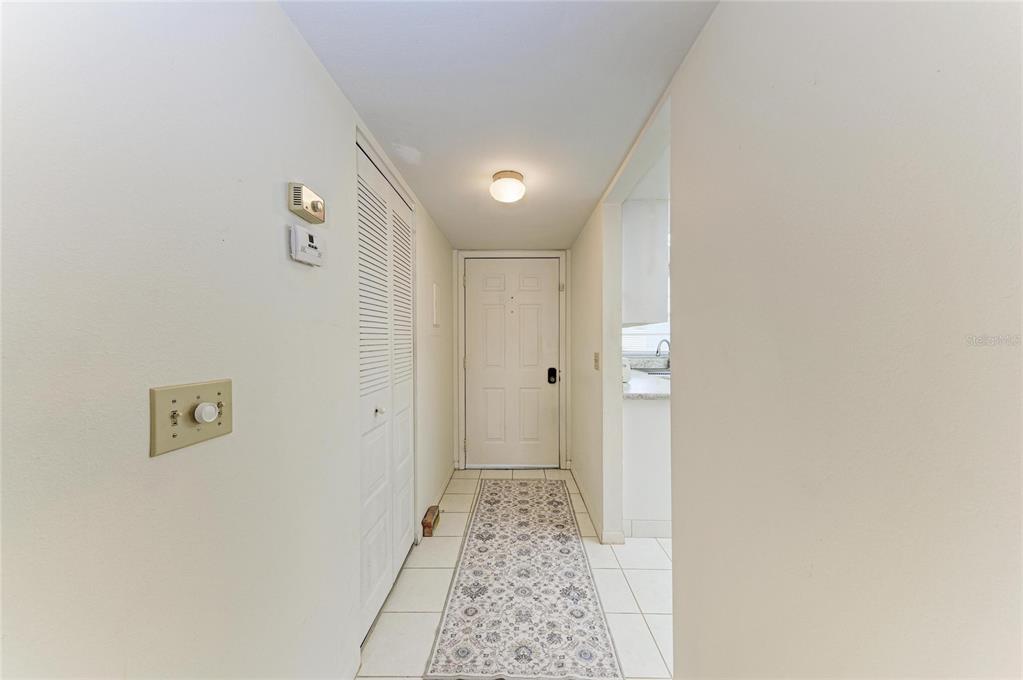 A hallway with white tile floors, a patterned runner rug, and a white entry door — 5962 7TH AVE W, BRADENTON, FL