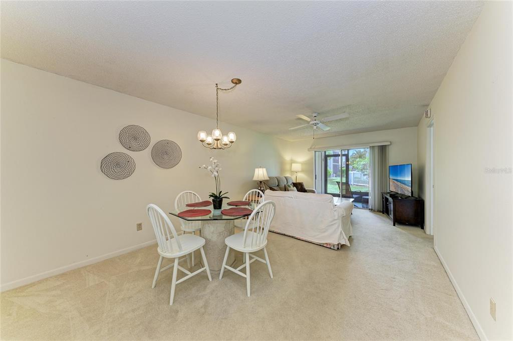 A dining area with a glass table and white chairs sits adjacent to a living room — 5962 7TH AVE W, BRADENTON, FL