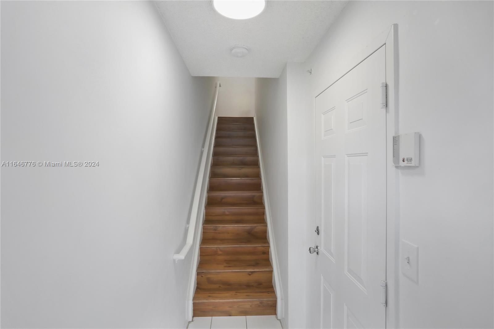 A narrow staircase with wood-look treads leads upward between two plain white walls — 2941 NE 185th St # 1305, Miami FL 33180, MIAMI, FL