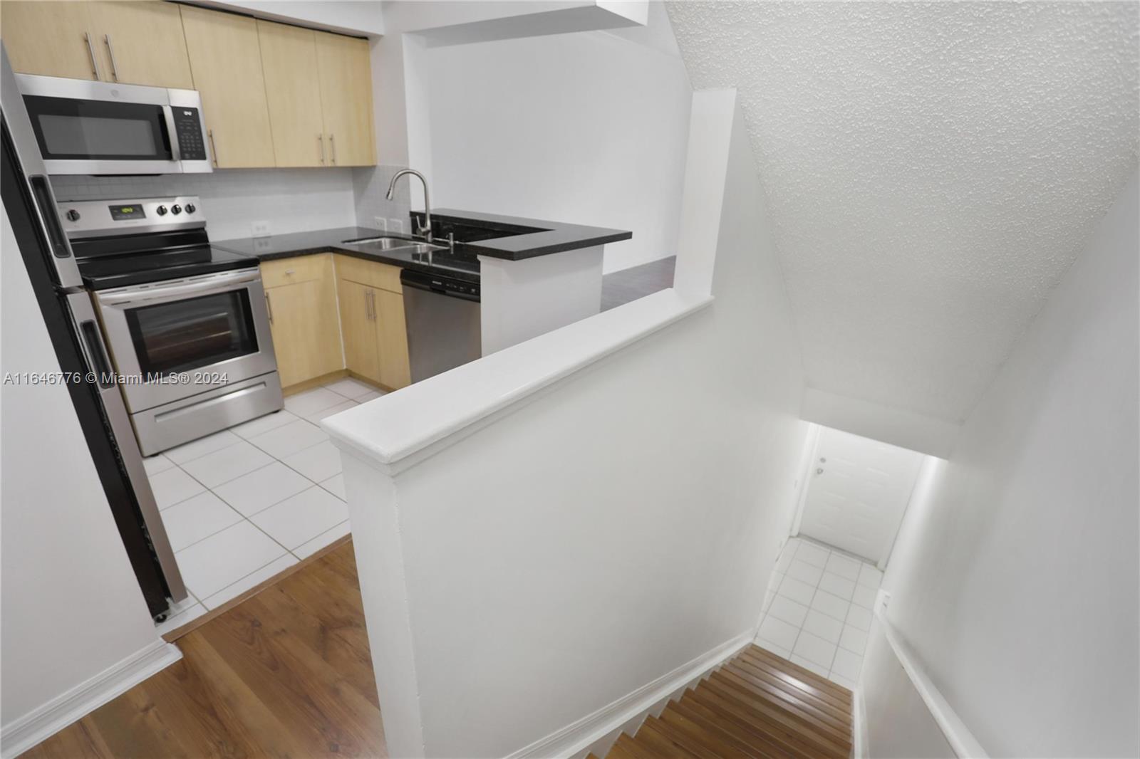 A kitchen with light wood cabinets and stainless steel appliances overlooks a staircase — 2941 NE 185th St # 1305, Miami FL 33180, MIAMI, FL