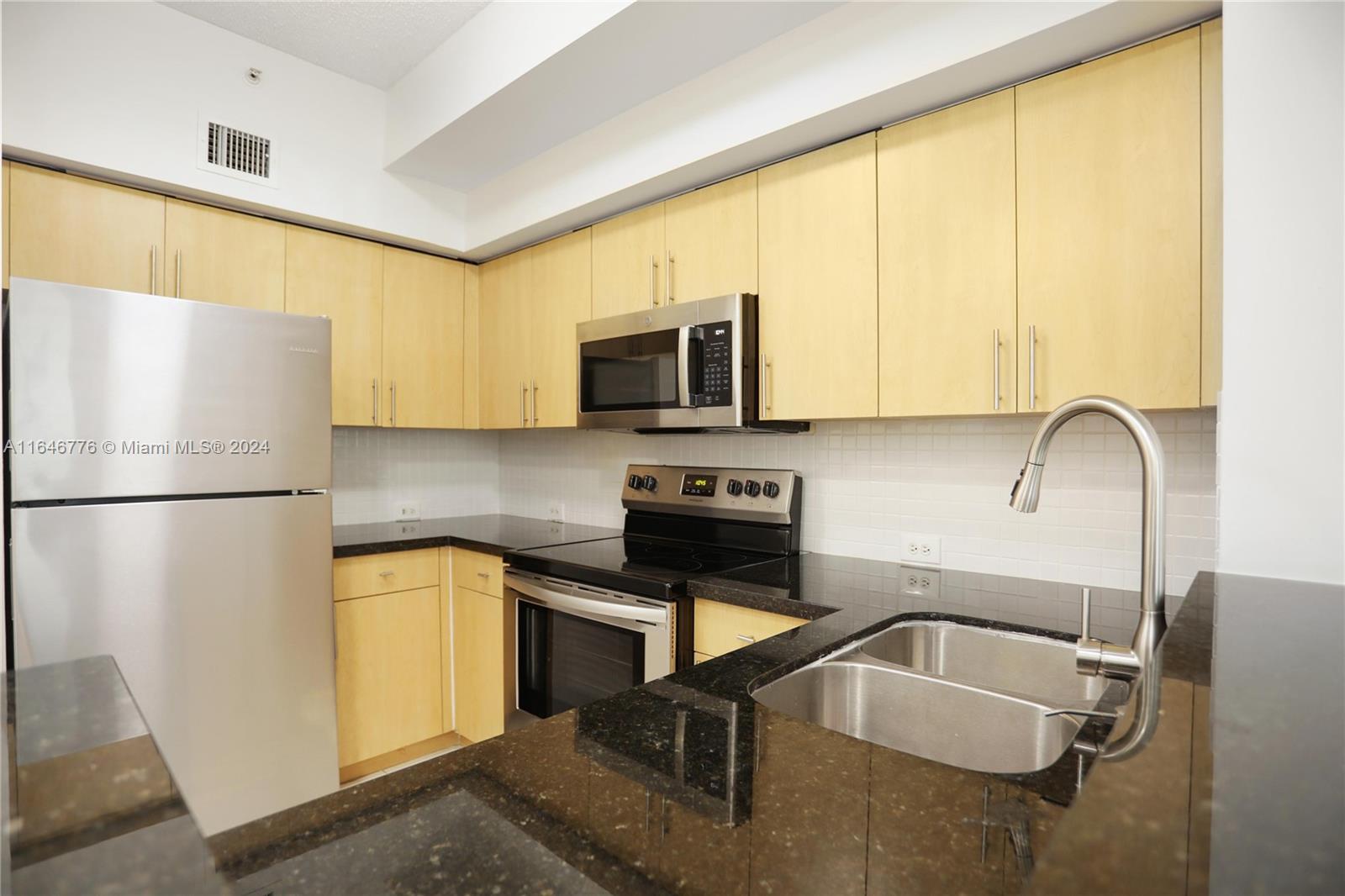 A kitchen features light wood cabinets, black granite countertops, stainless steel appliances, and white backsplash — 2941 NE 185th St # 1305, Miami FL 33180, MIAMI, FL