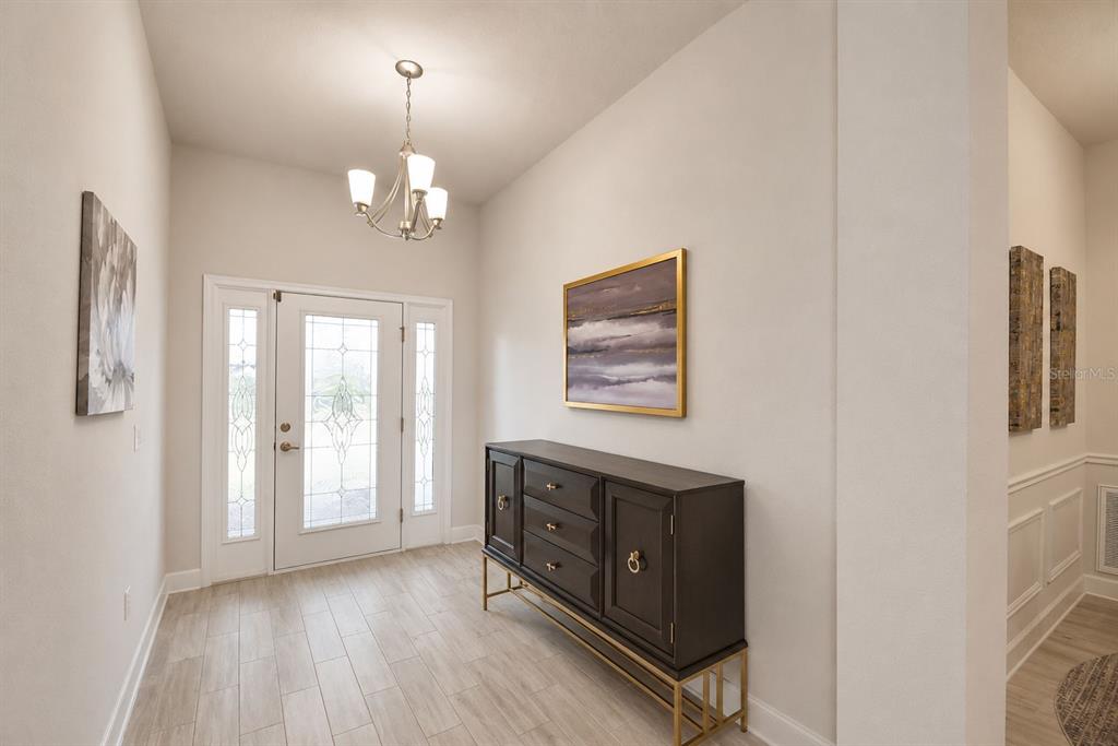A bright entryway features light wood-look tile flooring, a dark console table, and a chandelier — 4970 TENNESSEE LAKE DRIVE, AUBURNDALE, FL