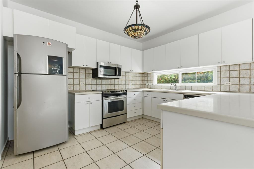 A kitchen features white cabinets, stainless steel appliances, tiled backsplash, and a tiled floor — B-6 VIA MORIZ ST. PASEO DEL MAR UNIT 434, DORADO, PR