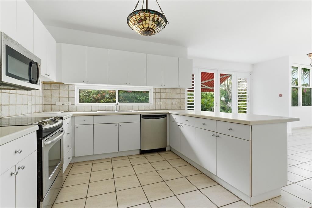 A kitchen with white cabinets, stainless steel appliances, tile flooring, and a stained-glass pendant light — B-6 VIA MORIZ ST. PASEO DEL MAR UNIT 434, DORADO, PR