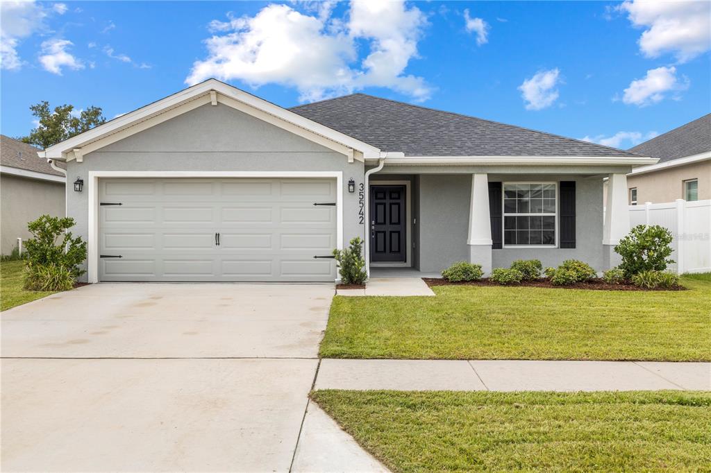 A single-story gray house with a two-car garage, front porch, and a manicured lawn — 35542 BELLINGTON BOULEVARD, ZEPHYRHILLS, FL